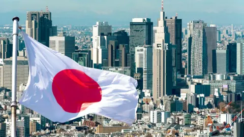 AFP via Getty Images A Japanese flag flies in front of the Tokyo skyline