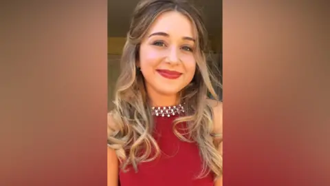 A selfie of a young girl with curly brunette hair wearing a red dress with a diamante collar and red lipstick.