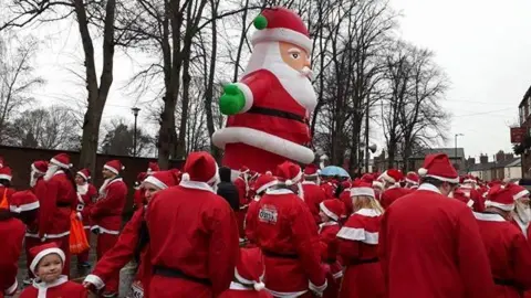 Dozens of people dressed in red and white Father Christmas outfits waiting to run. Some of them are wearing fake white beards.