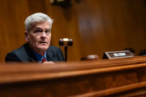 Getty Images Bill Cassidy, who has grey hair and a blue shirt with a red tie, holds a gavel during a hearing on Capitol Hill.