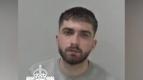 A custody image of Pirja after he was arrested. He looks at the camera and wears a grey jumper.