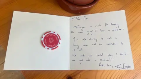 Paper Cup Cafe A red and white poker chip with the Envoy Casino printed on it on a card. The card to the Paper Cup Cafe thanks it for "keeping the crew going" and said the charity cafe was "an inspiration to all of us".