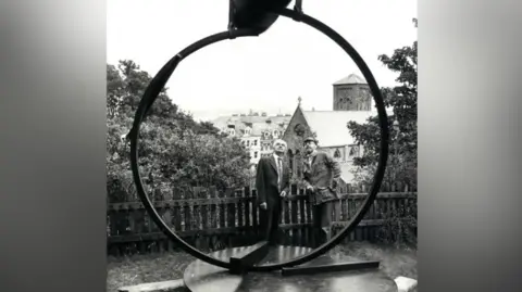Manx National Heritage Yn Arreyder is a large steel ring twisted to hold aloft a heavy double dome, positioned to look out across Douglas Bay towards the sunrise.
