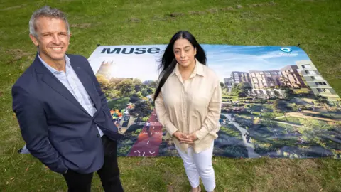 LDRS Muse Managing Director Phil Mayall And Oldham Council Leader Cllr Arooj Shah standing in front of a poster that shows the artist's impression of the cycle and pedestrian paths, leafy green trees and walkways