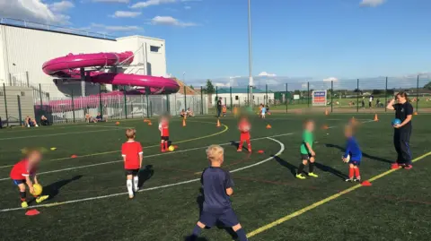 Greenbank FC Children taking part in football training on 3G pitches in front of One NK 