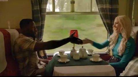 Ross and Ellie shaking hands over a train table en route to the castle