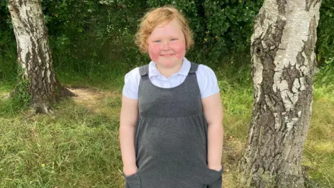 A young girl with ginger hair stood smiling 