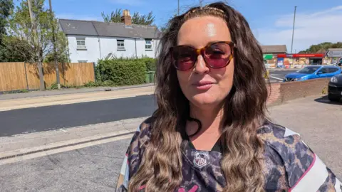Sarah Kenyon. She has long dark hair and is wearing a leopard print top and dark sunglasses. She is looking at the camera and smiling.