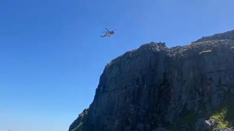 An air ambulance is pictured above a quarry in Derbyshire against a bright blue sky