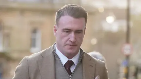 Former Scotland rugby captain Stuart Hogg in a light brown jacket with a grey-zipped top underneath and a purple tie. 