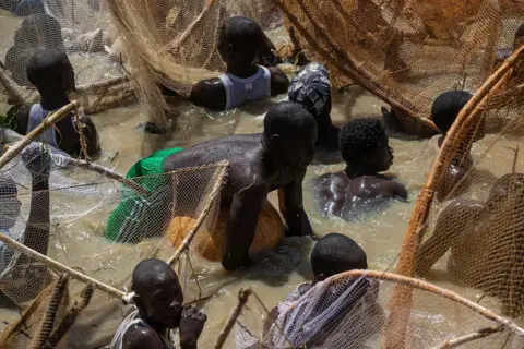 AFP via Getty Images A crowded picture of fishermen in the water with one in the middle floating on a gourd.
