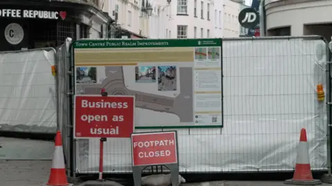 Metal gate with signs and a large banner on a white sheet covering the gate.