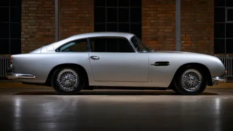 Dominic Fraser/Aston Martin Works The fully restored car with gleaming silver paint stands on the floor of a showroom