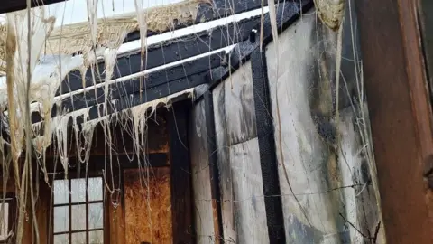 Plastic drips down from the ceiling. The walls are all burnt and charred.