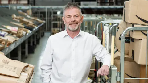 A man smiling standing in the postal equipment area.