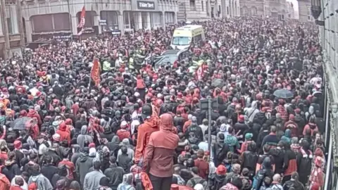 Still of video footage issued by Merseyside Police of Paul Doyle's car (top centre) being driven through a dense crowd of Liverpool supporters with an ambulance behind the vehicle on Water Street