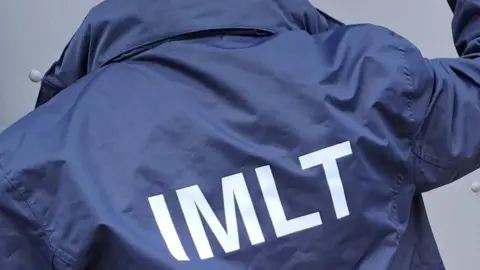 Illegal Money Lending Team A man wearing a blue jacket with white initials on it.