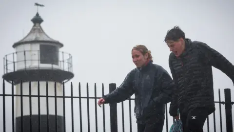 A man and a woman both wearing thick coats walk under the heavy rain past the lighthouse of the Southsea Castle, in Portsmouth.