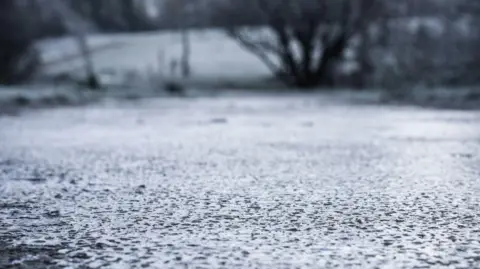 A road covered with ice. In the distance there are trees and fields also covered with ice.