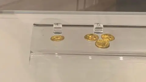 MICK LUNNEY/BBC Small gold coins in a display case
