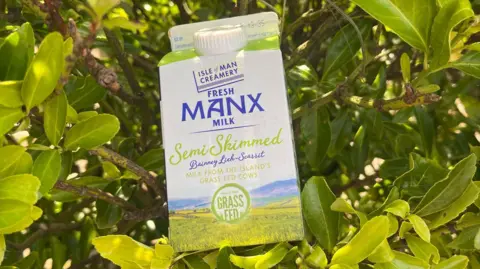 A pint of Manx milk with green labelling rests in front of a green bush.