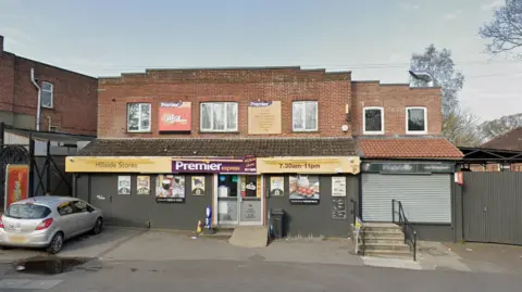 A general view picture of the two-storey building, with the shop on the ground floor, which has "Premier express" written on a yellow, purple and white sign. A Vauxhall car is parked outside the shop, to the left.