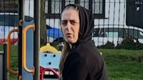 A woman in a black hoody standing in what appears to be a children's play park.