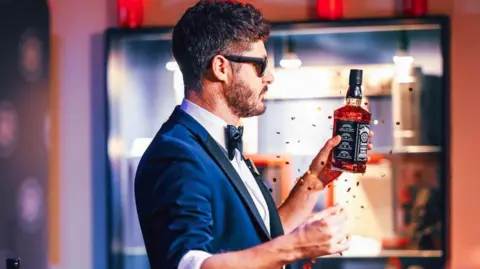 Mathew Knight with a whiskey bottle performing a magic trick