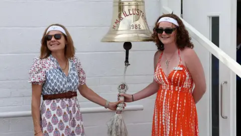 PA Media A mother and daughter both ringing a large bell attached to a white brick wall.