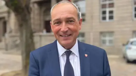 Senator Lyndon Farnham is pictured in the Royal Square. He is wearing a blue blazer and tie. 