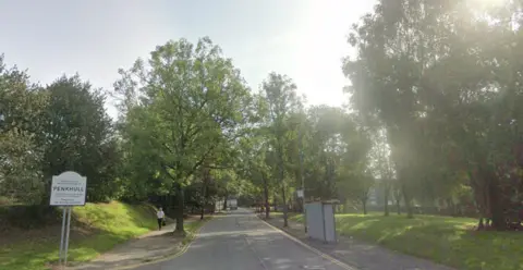 Google A Google street view showing a sign for Penkhull on the side of a main road. Grass and trees line the verges. A bus shelter is seen on the right pavement and a person walking towards the camera holding a bag on the left.