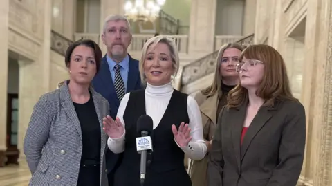 David Young/PA Wire Michelle O'Neill speaks to the media inside the Great Hall at Parliament Buildings, Stormont. She is surrounding by other Sinn Féin ministers including Infrastructure Minister Liz Kimmins, Finance Minister John O'Dowd, junior minister Aisling Reilly and economy minister Caoimhe Archibald