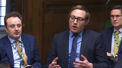 parliamentlive.tv Olly Glover, the Liberal Democrat MP for Didcot and Wantage, speaking at Prime Minister's Questions. He is wearing a blue suit, shirt and tie.