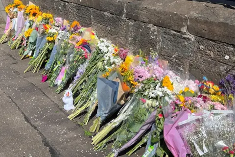 Bunches of flowers in a long line on a pavement near the scene of the incident