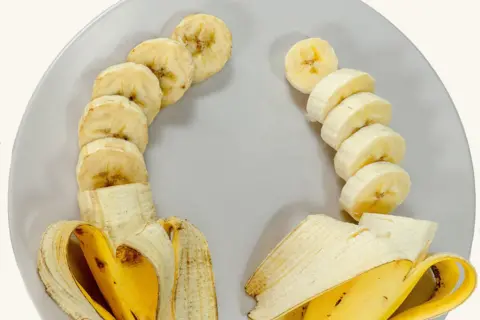 Tropic Two bananas side by side on a plate. They have both been peeled and cut into slices.