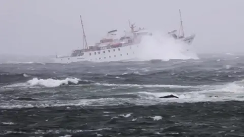 A white steamship sails through heavy seas , her bow is high as it hits a large wave.