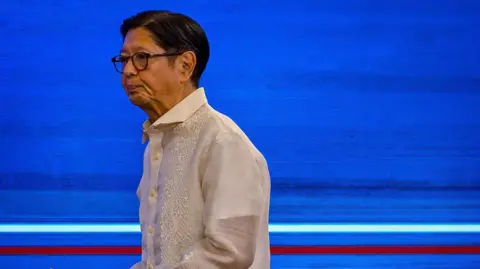 Philippine President Ferdinand Bongbong Marcos wearing a barong tagalog standing in front of a blue background