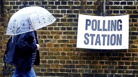 a person holding an umbrella over their head walks past a sign hanging from a wall which says Poling Station