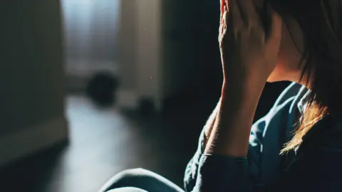 stock image of a young person with long hair holding their face in a dark room