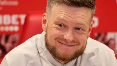 PA Media Middlesbrough manager Kim Hellberg speaks to the media during a press conference at Rockliffe Park Training Ground, Middlesbrough. He is smiling slightly. He has short brown hair and a beard, and is wearing a white sports top.