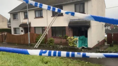 Scene of house fire in Dungannon - blackened windows and white and blue police tape