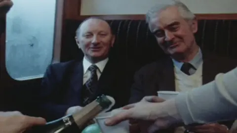 BBC A piece of archive film showing two businessmen on board a commuter train in 1980 being served champagne.