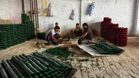 Neyaz Farooquee/BBC Four men sit and make dark green and red bangles in one of the factories in Firozabad