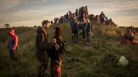 Getty Images People stood on a grassy hillside as a sun rises