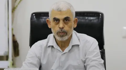 Getty Images A headshot of Yahya Sinwar, wearing a white shirt, sitting on a black leather chair and looking at the camera