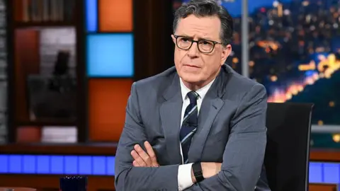 Colbert folding his arms as he broadcasts the June 25 show