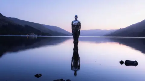 Robert McCrory An artistic sculpture of a man stands in a loch as the light dims