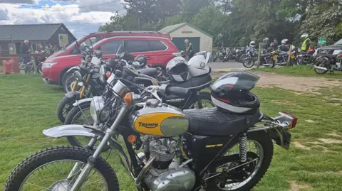 The View Coffee Shop Rows of motorbikes are parked on the grass in in front of the cafe. The nearest is a Triumph Trophy Trail with a yellow and chrome tank.