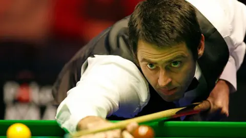 Getty Images A close-up of Ronnie O'Sullivan leaning over a green snooker table, resting his brown wooden cue on his hand.