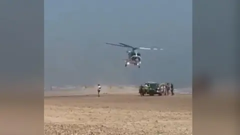 A helicopter lands on a sandy beach. 